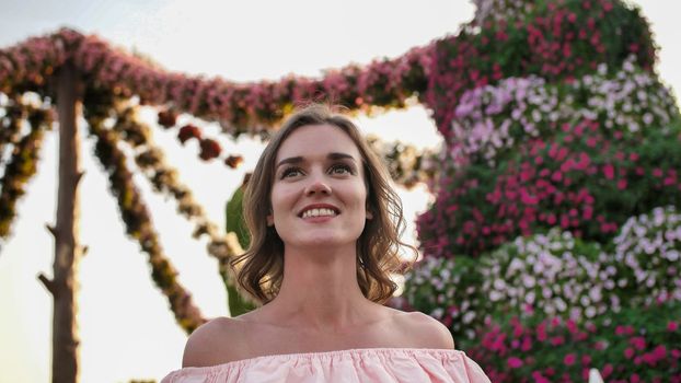 Girl on the background of hanging daisies of fresh flowers in a city park in Dubai