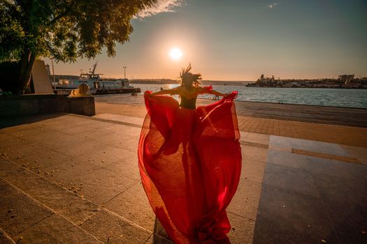 Sunrise red dress. A woman in a long red dress against the backdrop of sunrise, bright golden light of the sun's rays. The concept of femininity, harmony