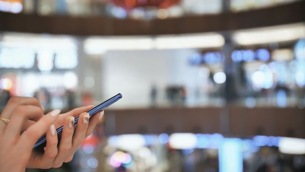 A girl in a shopping mall dials a message on the phone. Hands close up