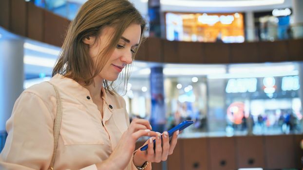 A girl in a shopping mall dials a message on the phone