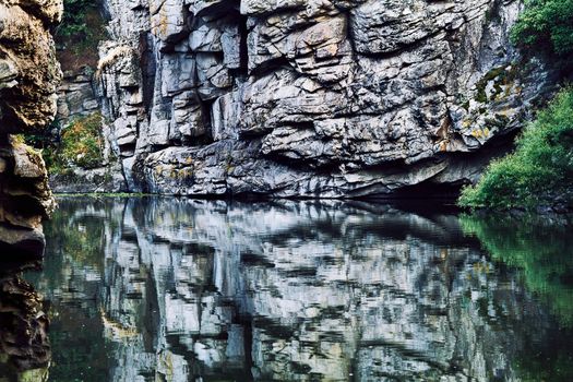 the solid mineral material forming part of the surface of the earth and other similar planets. Deep rocky silver canyon with smoothly flowing water and reflection close up.