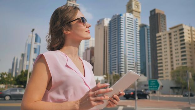 A girl works on a tablet against the background of skyscrapers of a metropolis