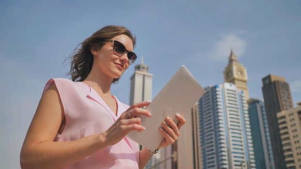 A girl works on a tablet against the background of skyscrapers of a metropolis