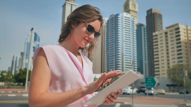 A girl works on a tablet against the background of skyscrapers of a metropolis