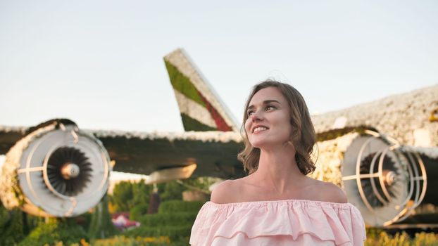 A girl admires in a city park on the background of an airplane of flowers