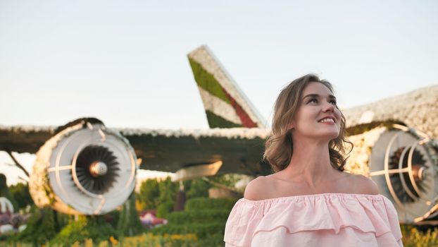 A girl admires in a city park on the background of an airplane of flowers