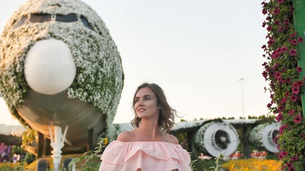 A girl admires in a city park on the background of an airplane of flowers