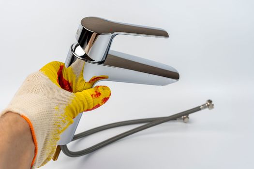 a shiny new sink faucet in the hand of a gloved plumber. Sink mixer before installation. Hot and cold water supply hoses are visible. the mounting screw for mounting is visible.