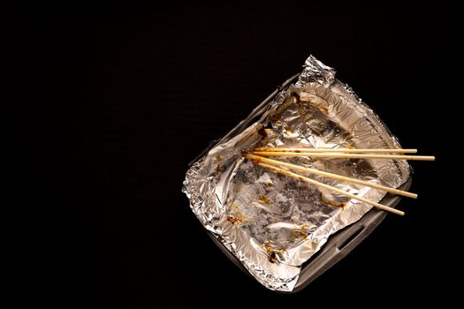 An empty plastic container for the delivery of a set of sushi. Chopsticks and an empty thermobox with foil inside for a set of sushi on a dark background. lunch. View from above. Flat lay. Copy space