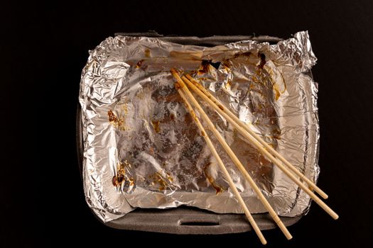 An empty plastic container for the delivery of a set of sushi. Chopsticks and an empty thermobox with foil inside for a set of sushi on a dark background. lunch. View from above. Flat lay. Copy space. close-up