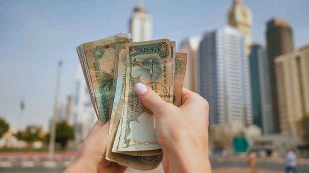 Hands of a girl holding money of the United Arab Emirates on the background of Dubai skyscrapers