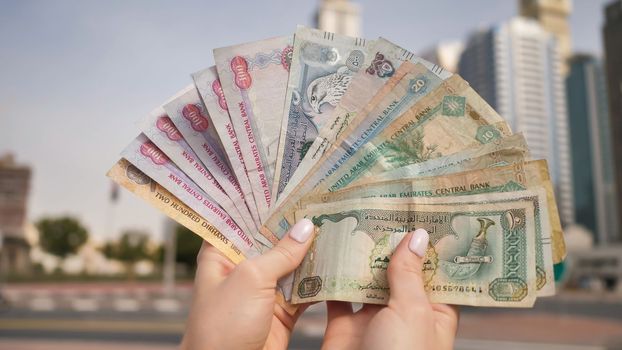 Hands of a girl holding money of the United Arab Emirates on the background of Dubai skyscrapers
