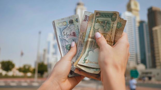 The girl holds in her hands the money of the United Arab Emirates on the background of the city center of Dubai