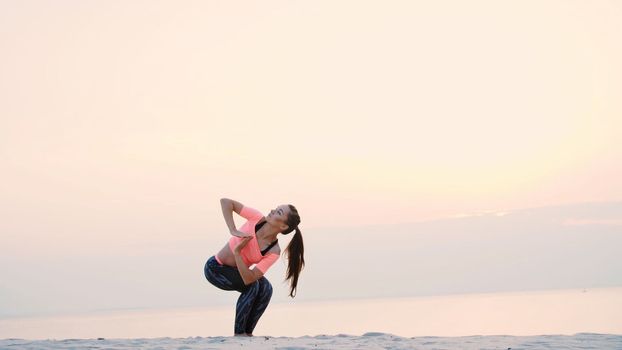 Healthy, young beautiful woman meditating, practicing yoga on the sea beach, at sunrise, Makes exercises for balance and coordination, deep muscle tone. High quality photo