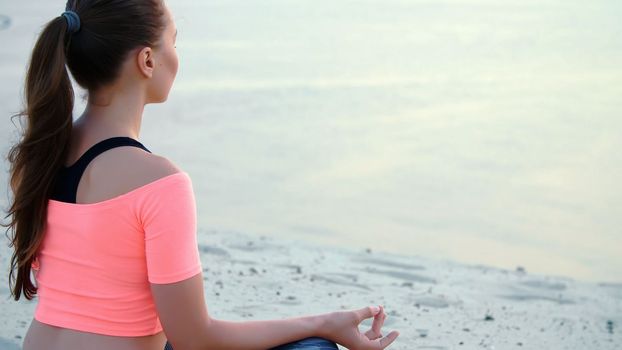 Woman sitting in relaxation yoga pose at the sea beach. Closeup. High quality photo