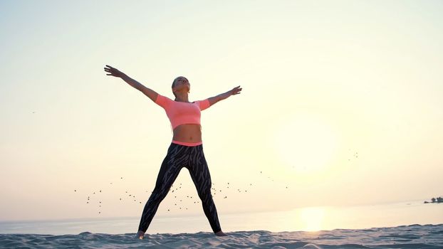 Healthy, young beautiful woman meditating, stretching, practicing yoga on the sea beach, at sunrise, Makes exercises for balance and coordination, deep muscle tone. High quality photo