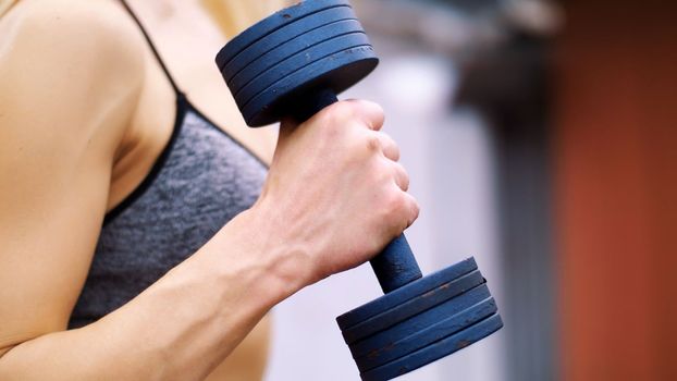 Beautiful sexy athletic young blond woman in top, shorts, engaged in crossfit, performs various strength exercises with dumbbells, close-up on the side, bottom, slow motion. High quality photo