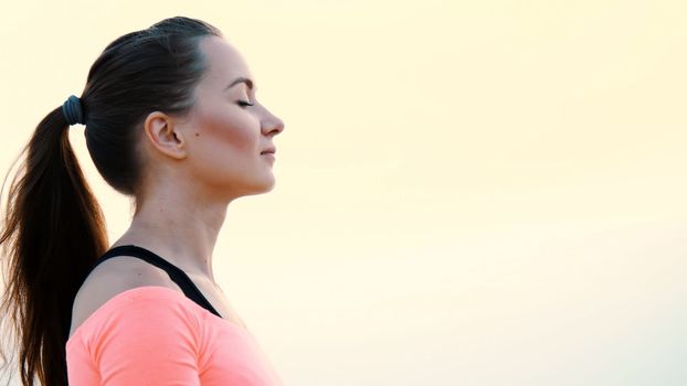 Healthy, young beautiful woman meditating, practicing yoga among the sand, on the beach, by the sea, river, at dawn, at sunrise, closeup.