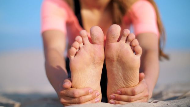 Beautiful blond woman doing stretching exercises on the beach. Close-up of foot. High quality photo