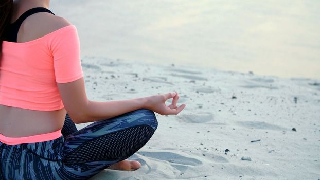 Woman sitting in relaxation yoga pose at the sea beach. Closeup. High quality photo