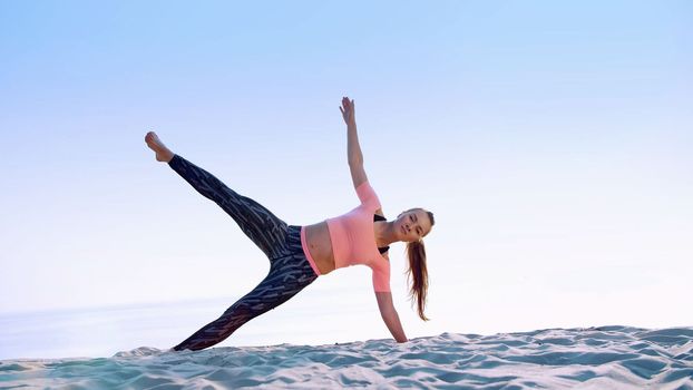 Healthy, young beautiful woman doing exercises for oblique abdominal press muscles,, on the beach, at sunrise, Makes exercises for balance and coordination, deep muscle tone. High quality photo