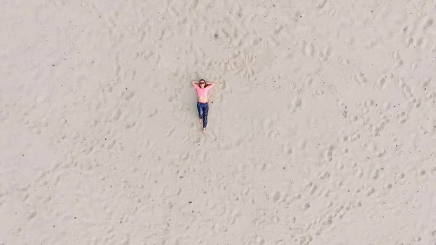 Stylish young athletic beautiful woman in sunglasses, lying on the sand, on a deserted beach, in summer. View from above, aero video. High quality photo