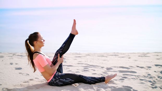 Healthy, young beautiful woman performs exercises for muscles of the press, picks up the body, legs, pumps the press lying on the sand, on the beach, at sunrise. High quality photo