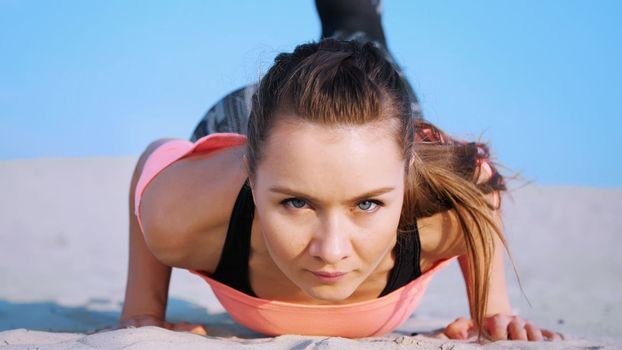 Healthy, young beautiful woman doing, performs push-ups,on the beach, at sunrise, Makes exercises for balance and coordination, deep muscle tone. Close-up, portrait. High quality photo
