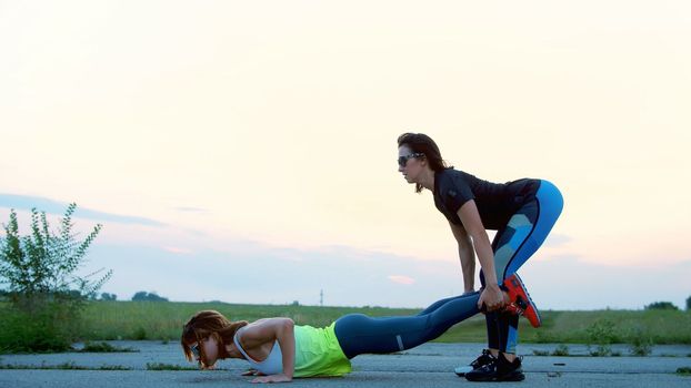Beautiful, athletic, young women in sunglasses, in tights, perform synchronously strength exercises, exercises in pairs, as an additional weight. on an abandoned airfield, sunset. High quality photo