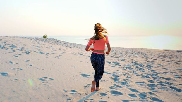 Healthy, young sports beautiful woman runs along the sand, on the beach, in summer, towards the sun, at the sunrise. High quality photo