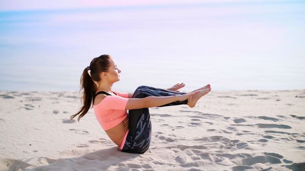 Healthy, young beautiful woman performs exercises for muscles of the press, picks up the body, legs, pumps the press lying on the sand, on the beach, at sunrise. High quality photo