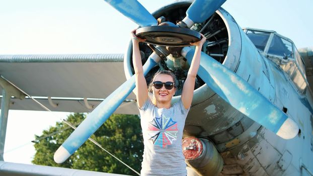 at sunset, athletic, young woman in sunglasses, in tights, doing exercises with weight, heavy weight plate, on an abandoned airfield, against the background of an old plane,. High quality photo