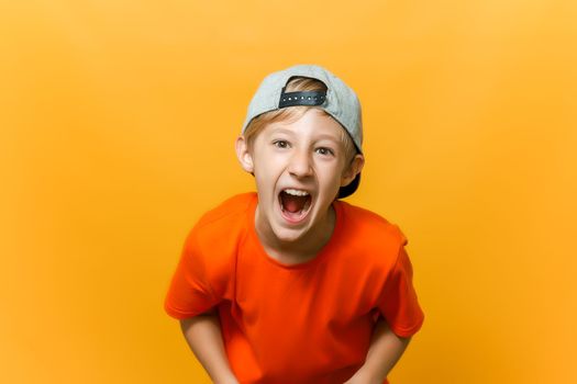 a computer gamer boy on a yellow background shows emotions. a child in a cap and an orange T-shirt is playing a game station