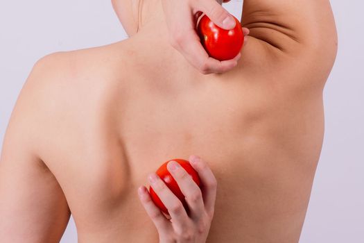 Healthy young woman holding a tomatos over her eyes, laughing, bare shoulders, topless.