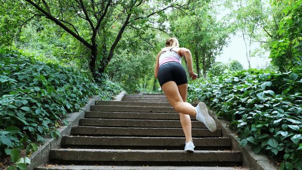 Beautiful sexy athletic young blond woman runs upstairs, in the forest, park, in summer day. Performs exercises to strengthen the different muscles of the legs on the stairs. High quality photo