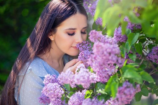 Beautiful brunette girl, with long hair, smells lilac flowers, in the summer in the park, sunny day. Close up