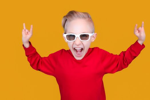 a cool and cheerful child in red clothes and glasses shows hand gestures on a yellow background