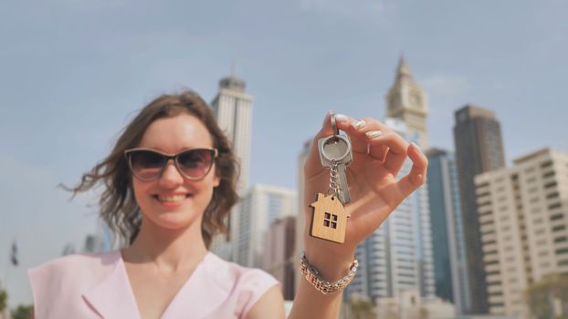 Real estate purchase concept. The girl holds the keys to a new house on the background of a Dubai skyscraper