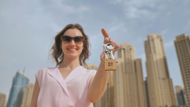 The concept of buying an apartment. Girl holds the keys to a new house against the backdrop of skyscrapers in the city