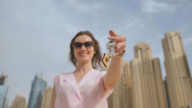 Real estate purchase concept. The girl holds the keys to a new house on the background of a Dubai skyscraper