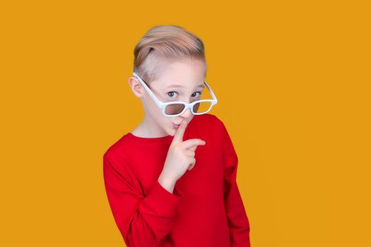 a cheerful child in children's 3D glasses puts his index finger to his lips and makes a quiet gesture