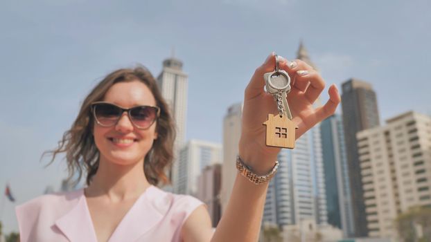 Real estate purchase concept. The girl holds the keys to a new house on the background of a Dubai skyscraper