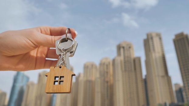 Real estate purchase concept. The girl holds the keys to a new house on the background of a Dubai skyscraper