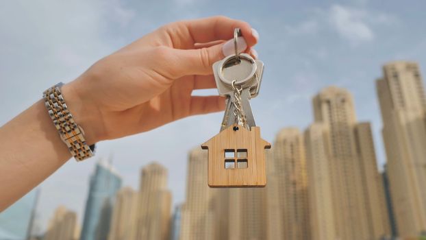 Real estate purchase concept. The girl holds the keys to a new house on the background of a Dubai skyscraper
