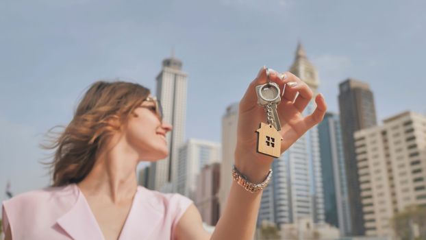 The concept of buying an apartment. Girl holds the keys to a new house against the backdrop of skyscrapers in the city