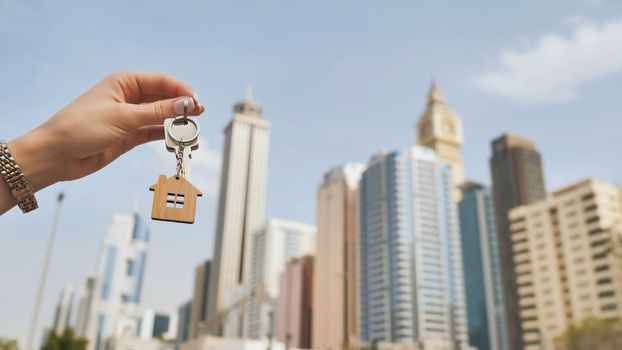 Real estate purchase concept. The girl holds the keys to a new house on the background of a Dubai skyscraper