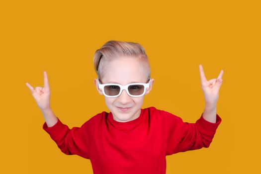a cool and cheerful child in red clothes and glasses shows hand gestures on a yellow background
