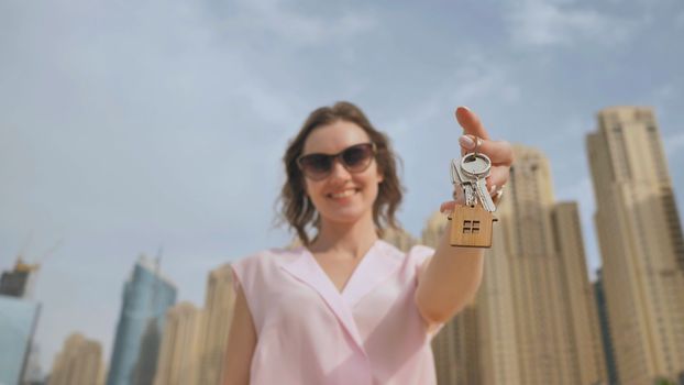 The concept of buying an apartment. Girl holds the keys to a new house against the backdrop of skyscrapers in the city
