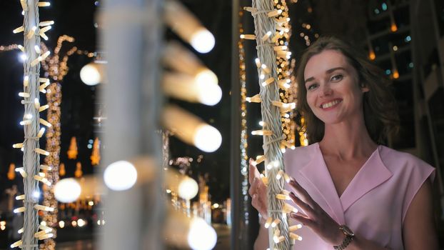 The girl gently touches the glowing lights on a palm tree in the night city of Dubai
