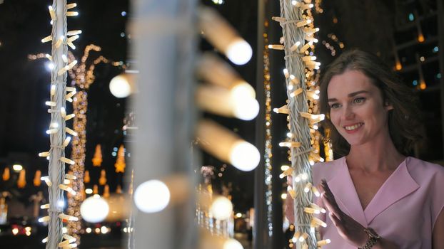 The girl gently touches the glowing lights on a palm tree in the night city of Dubai
